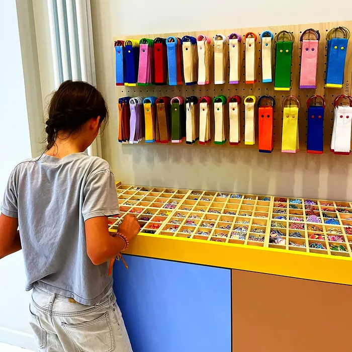 Une enfant fouille les boîtes d'écussons thermocollants rangées sur le comptoir jaune et violet de l'atelier