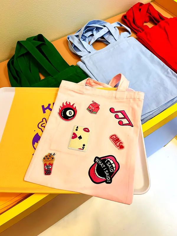 Deux tote bags personnalisés avec des écussons brodés, posés sur le comptoir de l'Atelier Kitsu