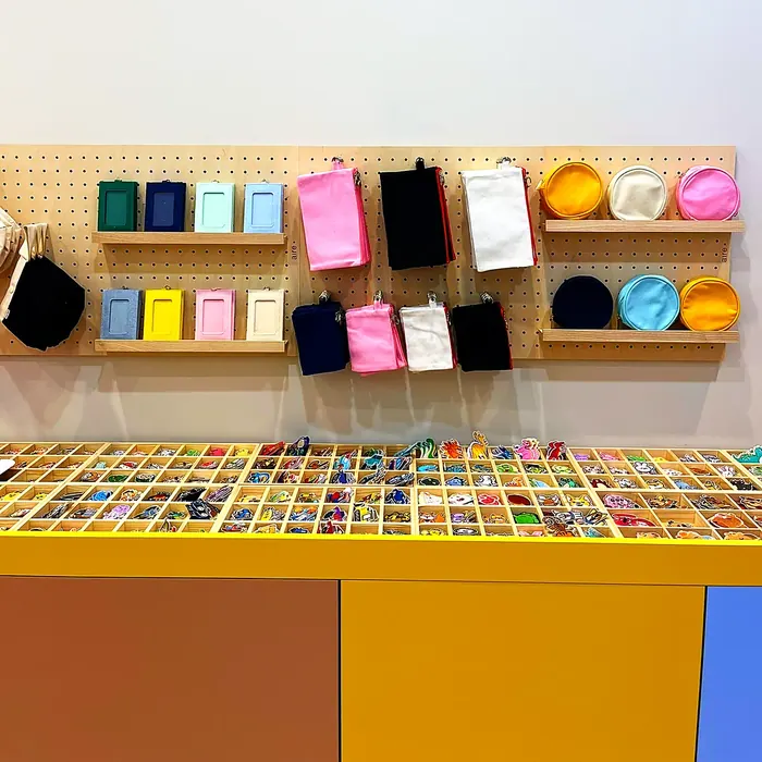Le mur d'accessoires de l'Atelier Kitsu : tote bags, pochettes et porte-clés de toutes les couleurs, au-dessus des boîtes d'écussons